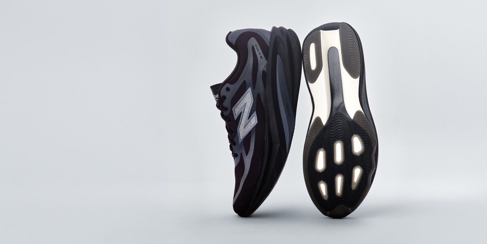 A pair of black New Balance sneakers sitting on a gray studio backdrop.